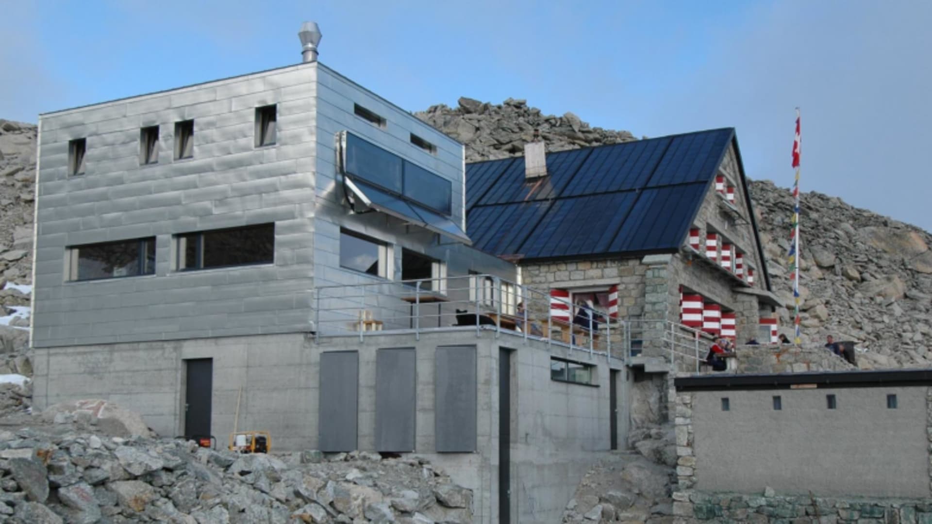 Außenansicht der Cabane du Trient mit modernem Metallbau und traditionellem Steingebäude mit Schweizer Flagge.