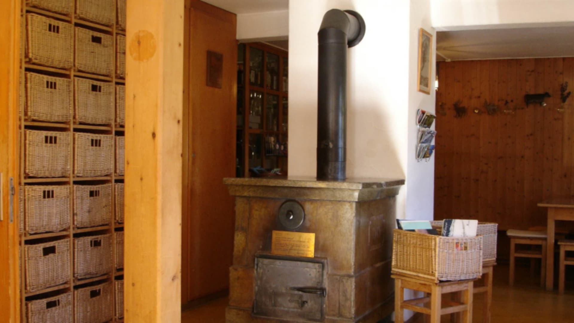 Gemeinschaftsraum der Chamonna Tuoi mit zentralem Steinofen und rustikaler Holzeinrichtung.