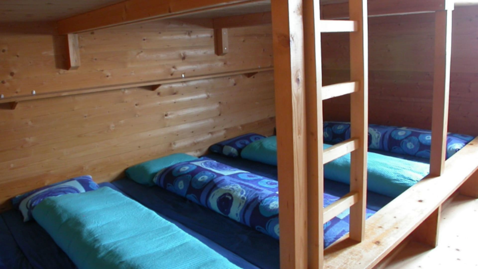 Schlafsaal der Chamonna Tuoi mit Holz-Etagenbetten und türkisfarbener Bettwäsche.