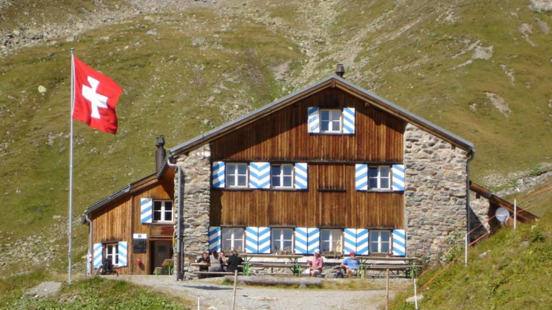 Bergwanderer pausieren vor der Chamonna Tuoi bei traditioneller Schweizer Berghütten-Architektur.