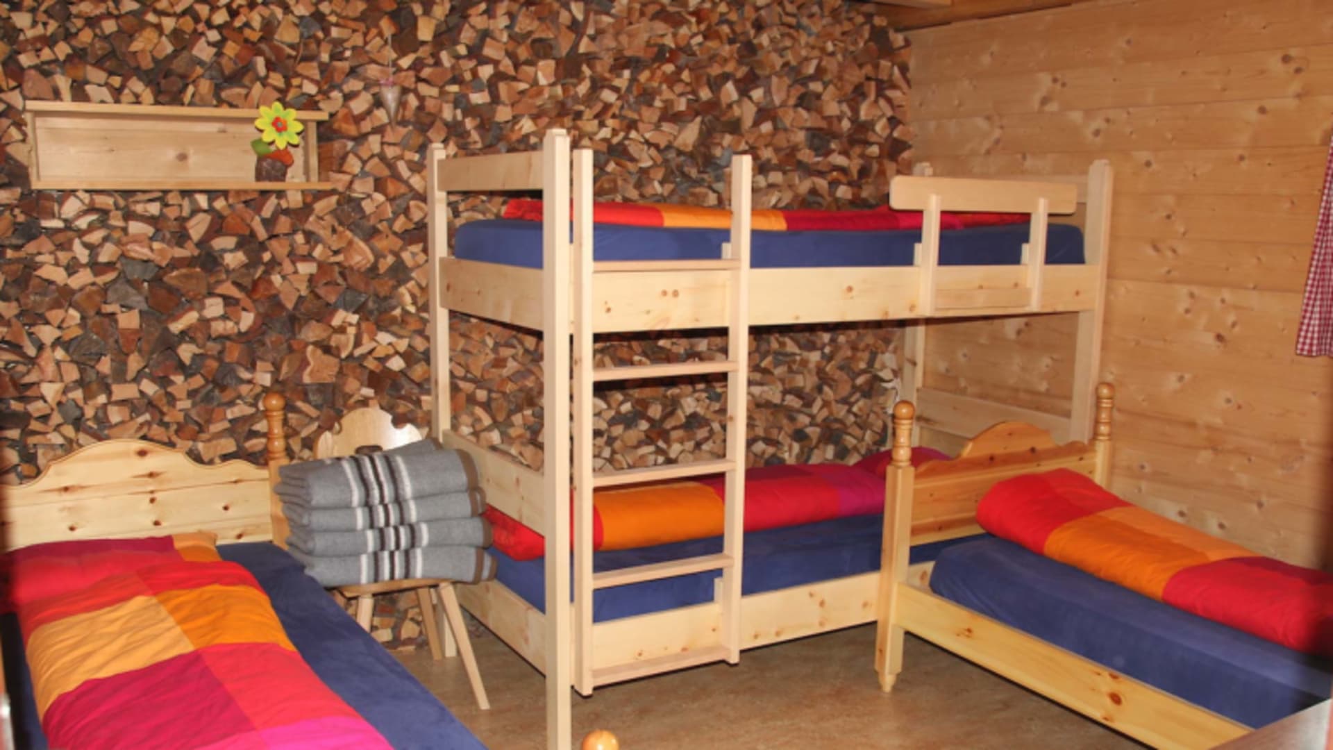 Familienzimmer der Chamanna Jenatsch mit vier Holzbetten und bunten Bettbezügen in traditioneller Holzbauweise.