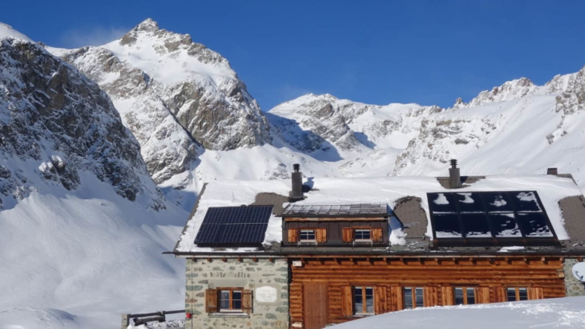 Die Chamanna Jenatsch steht im tiefen Pulverschnee vor einem Panorama schneebedeckter Felswände.