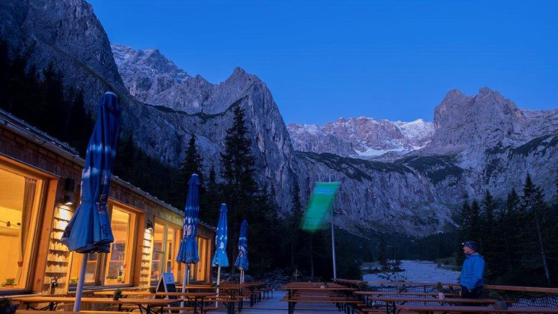 Höllentalangerhütte in der blauen Stunde mit beleuchteten Fenstern vor schneebedeckten Gipfeln des Wettersteingebirges.