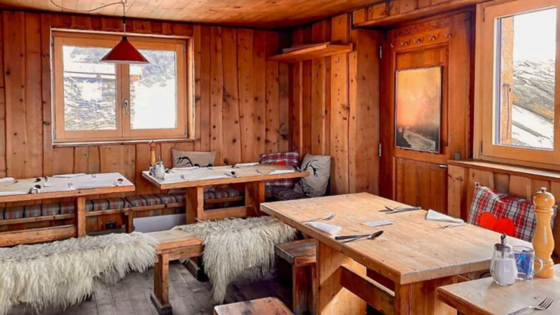 Gastraum der Gandegghütte mit holzvertäfelten Wänden, gedeckten Tischen und Blick auf die Berge.