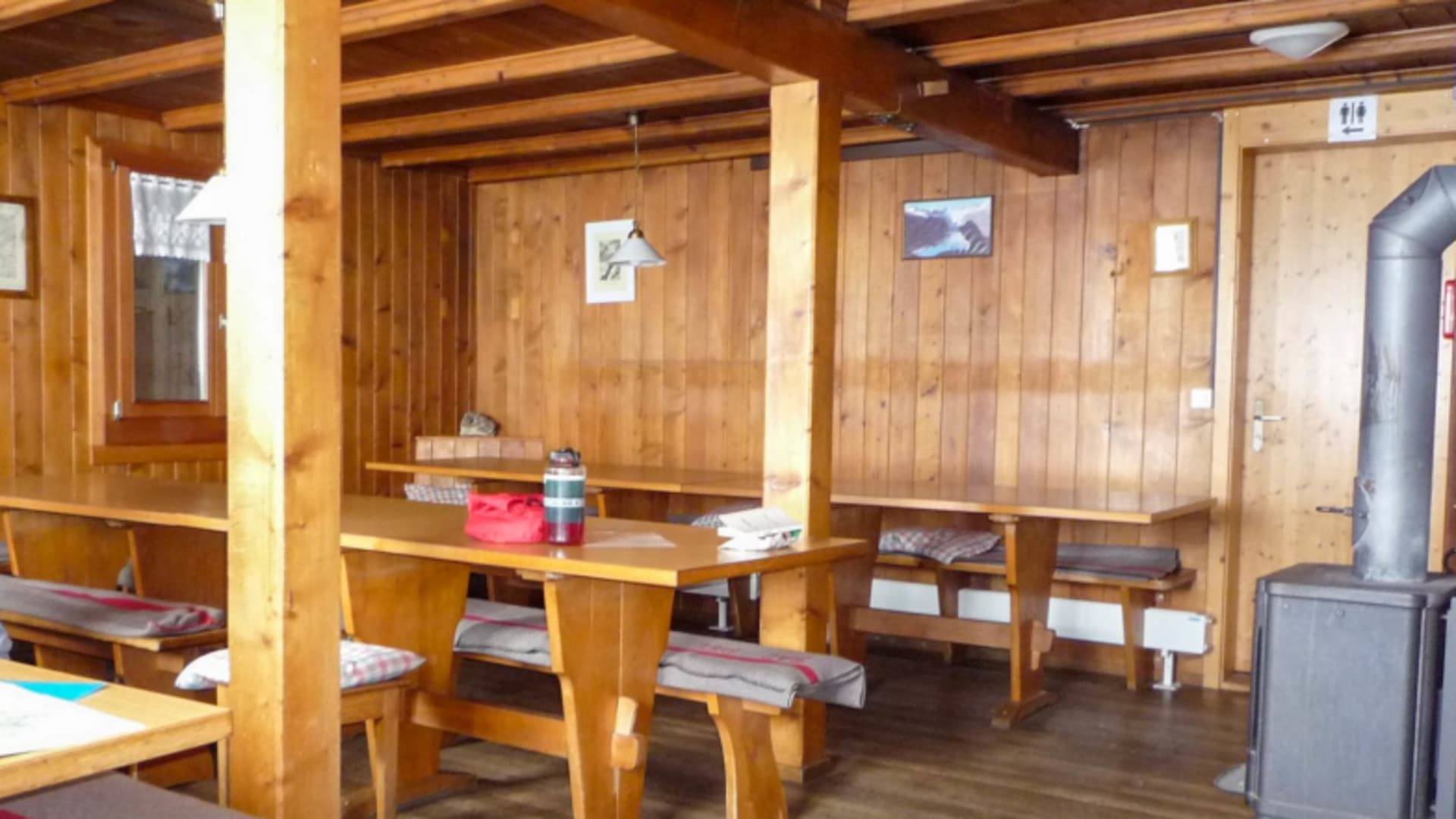 Gastraum der Oberaarjochhütte mit Holztischen, rot-weiß karierten Kissen und traditioneller Holzvertäfelung.