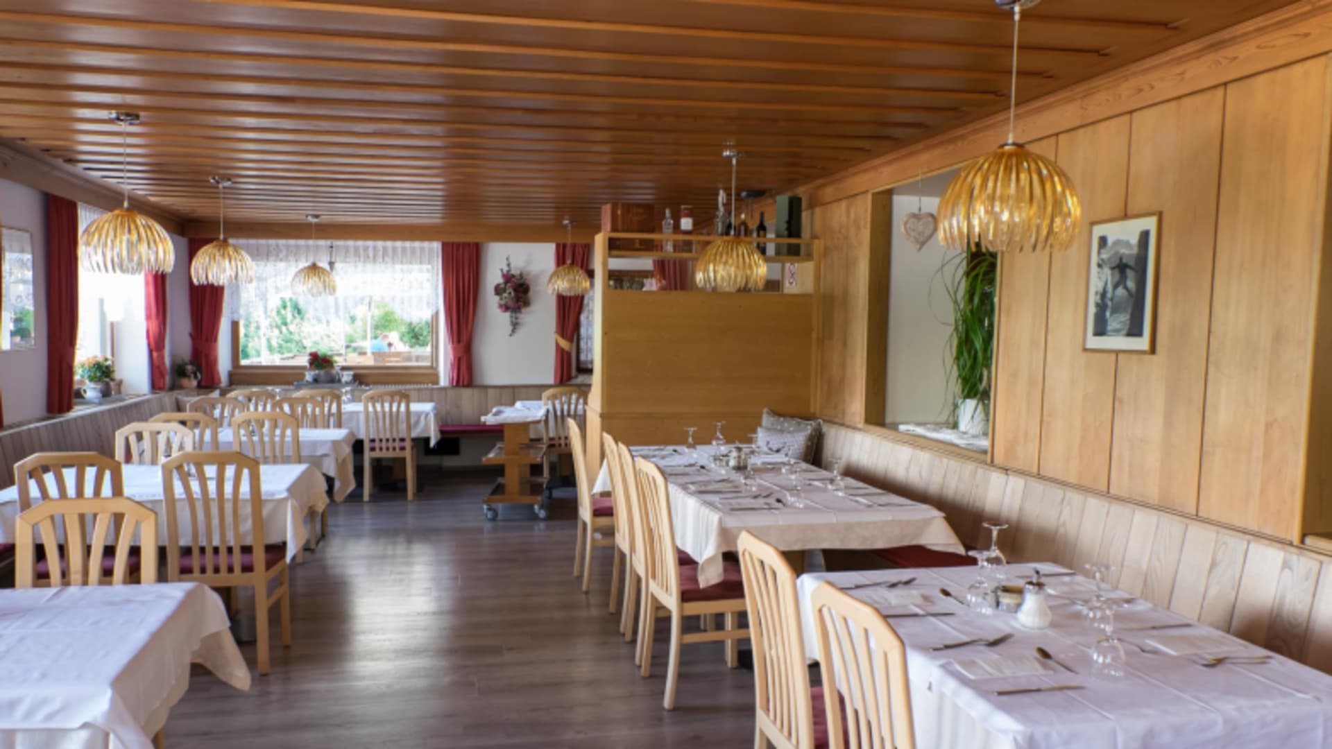 In der Gaststube des Restaurant Frara hängen runde Holzpendelleuchten über gedeckten Tischen mit hellen Holzstühlen.