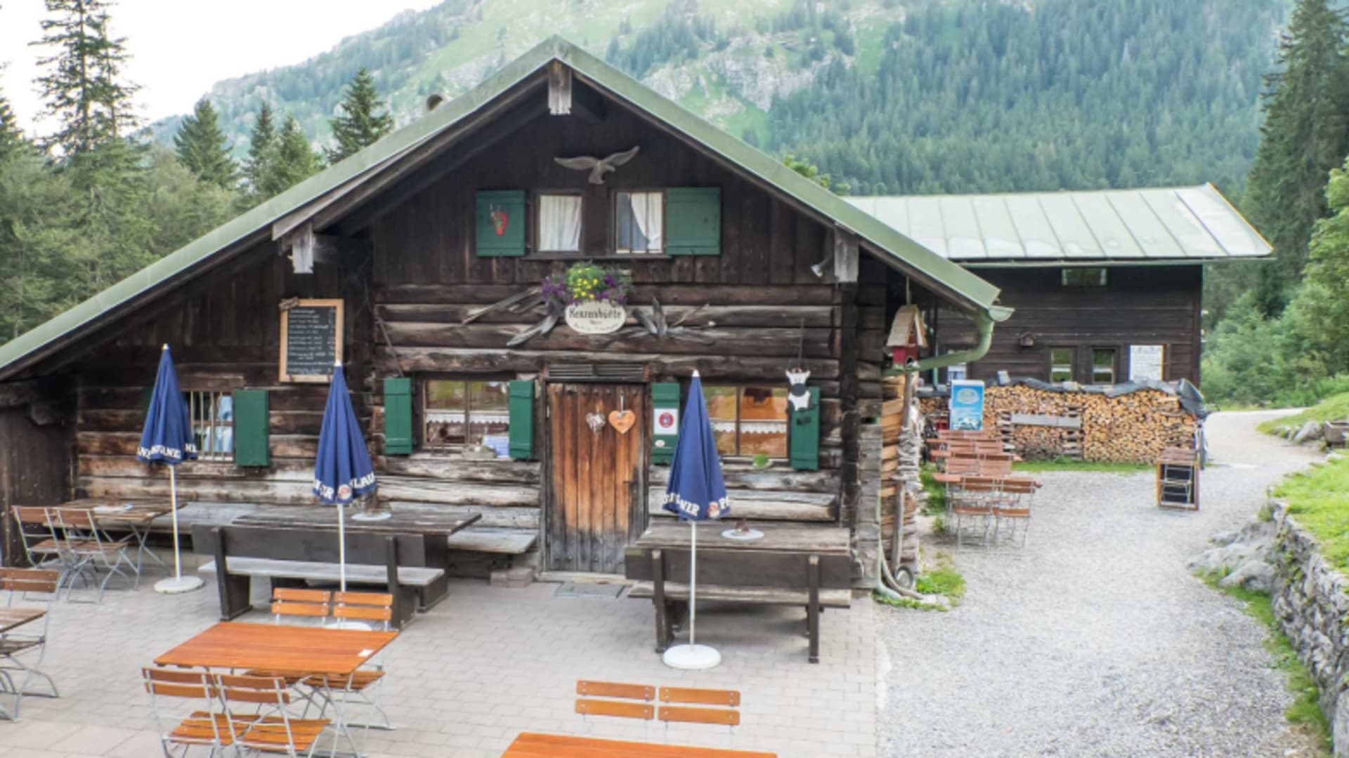 Die Kenzenhütte auf 1.294 m mit großer Holzterrasse und blauen Sonnenschirmen im grünen Tal.