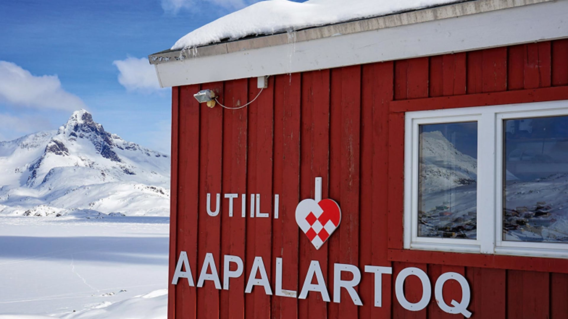 Fassade des The Red House, Tasiilaq (Ostgrönland) mit verschneitem Felsgipfel im Hintergrund.