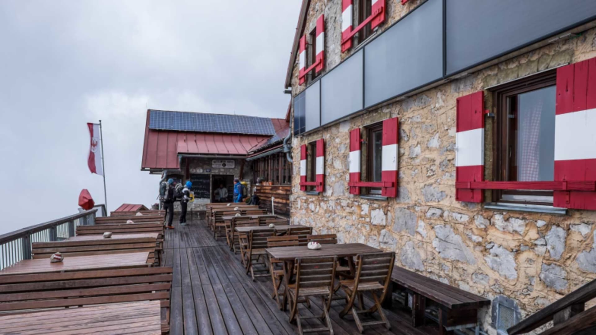 Holzterrasse der Bettelwurfhütte mit Tischen und Bänken im Biergartenstil für Wanderer und Gäste.