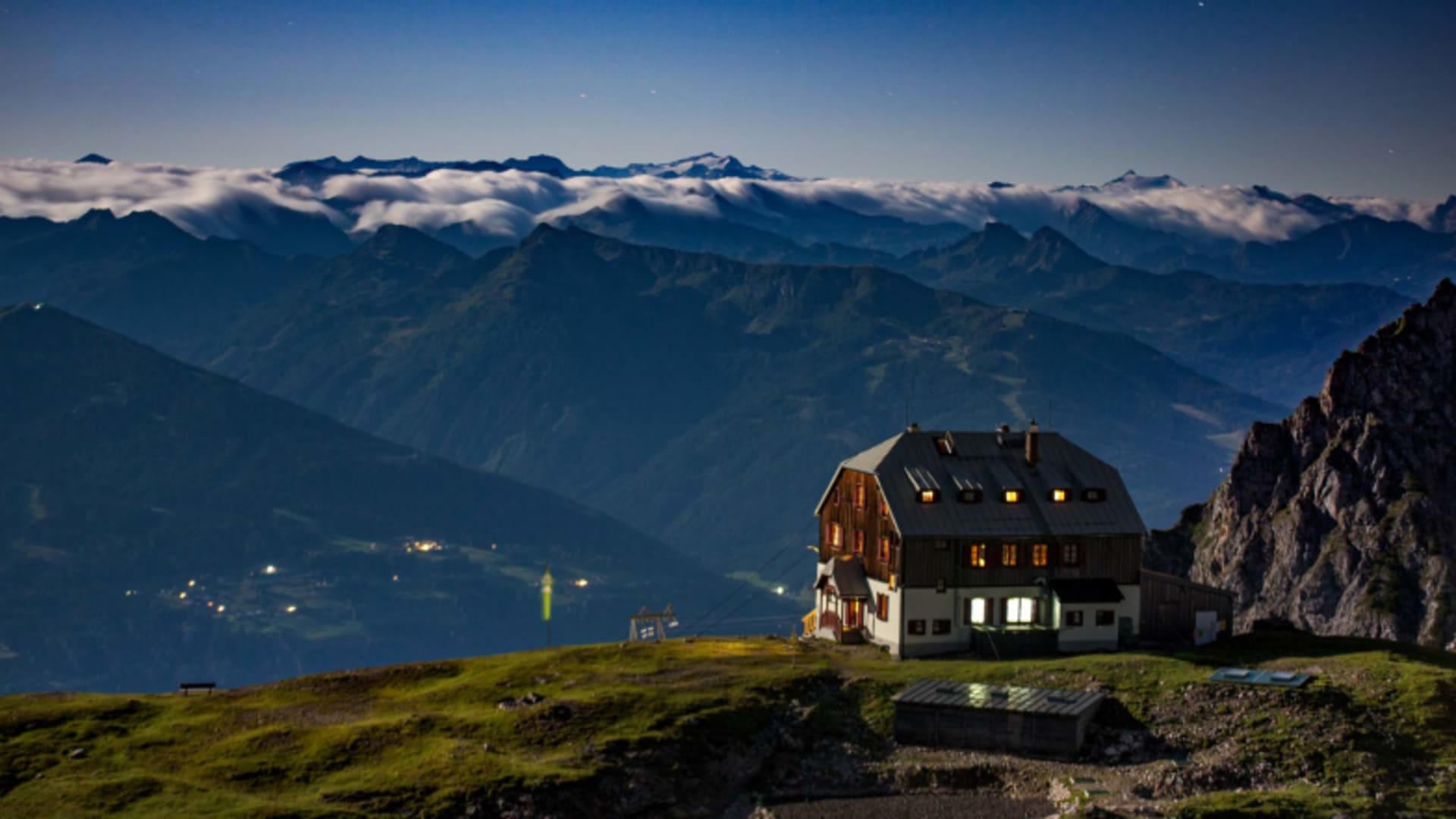 Das beleuchtete Guttenberghaus auf Almwiese bei Dämmerung mit ersten Sternen am Himmel.