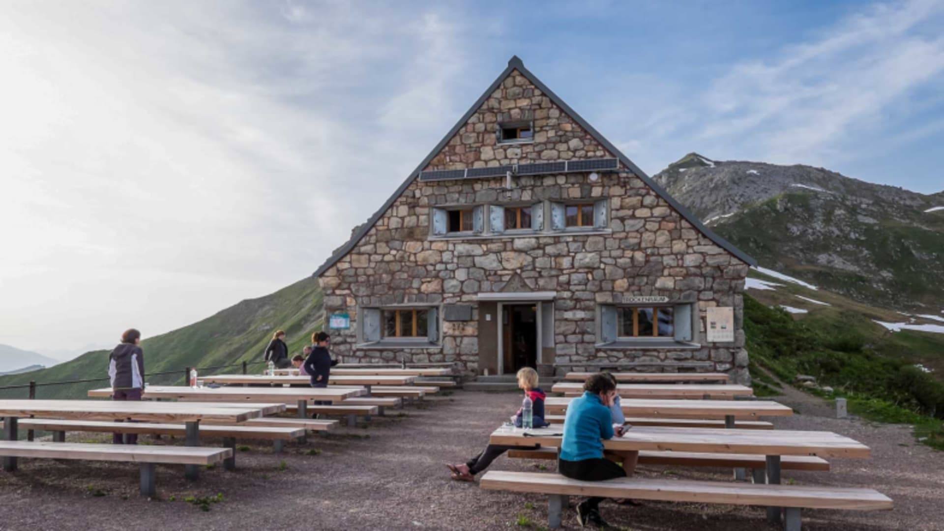 Bergsteiger sitzen auf der Sonnenterrasse der Pfälzerhütte bei warmer Abendstimmung.