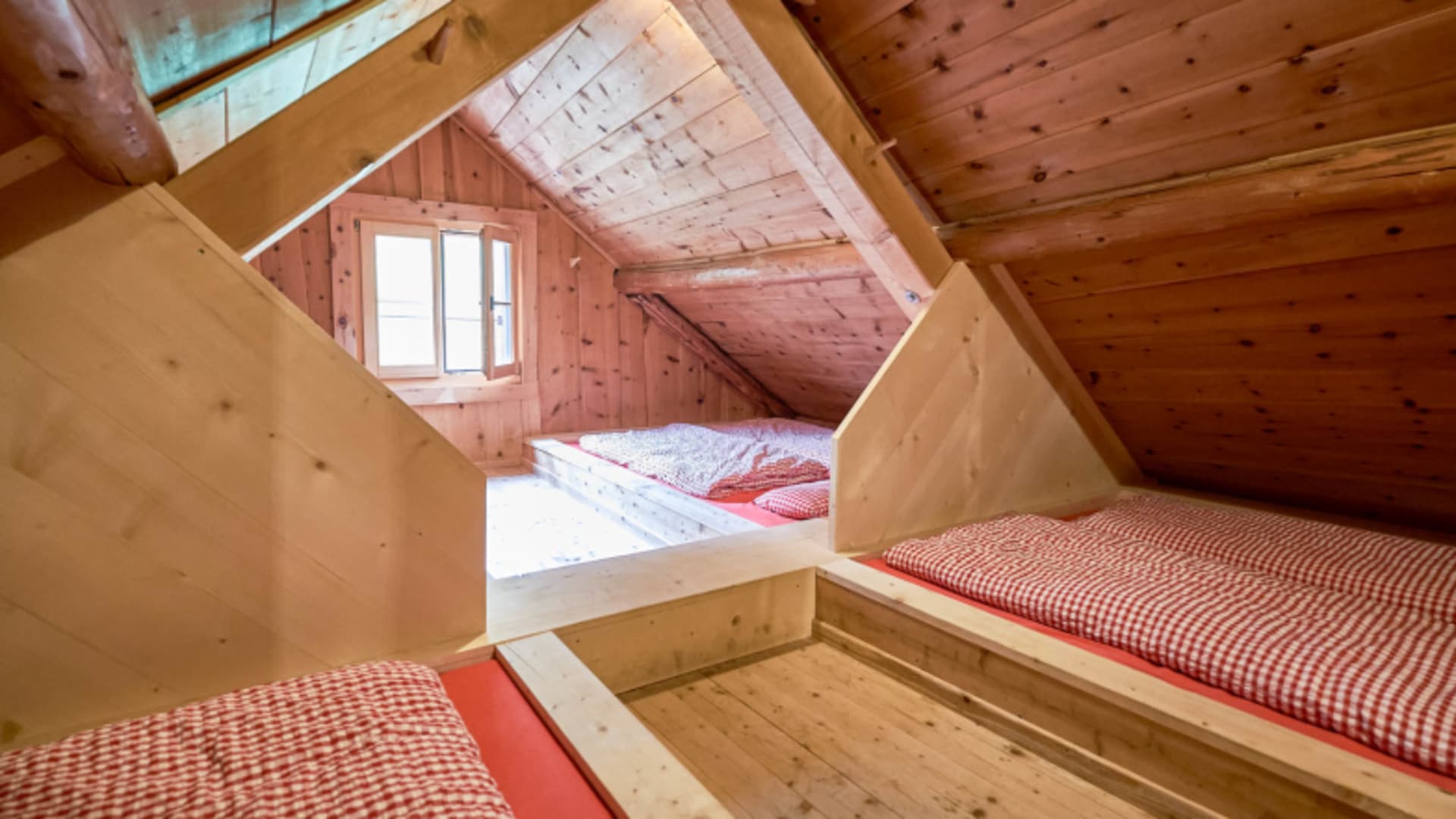 Drei eingebaute Holzbetten mit rot-weiß karierten Bezügen im Dachgeschoss-Schlafraum der Chamanna Cluozza.