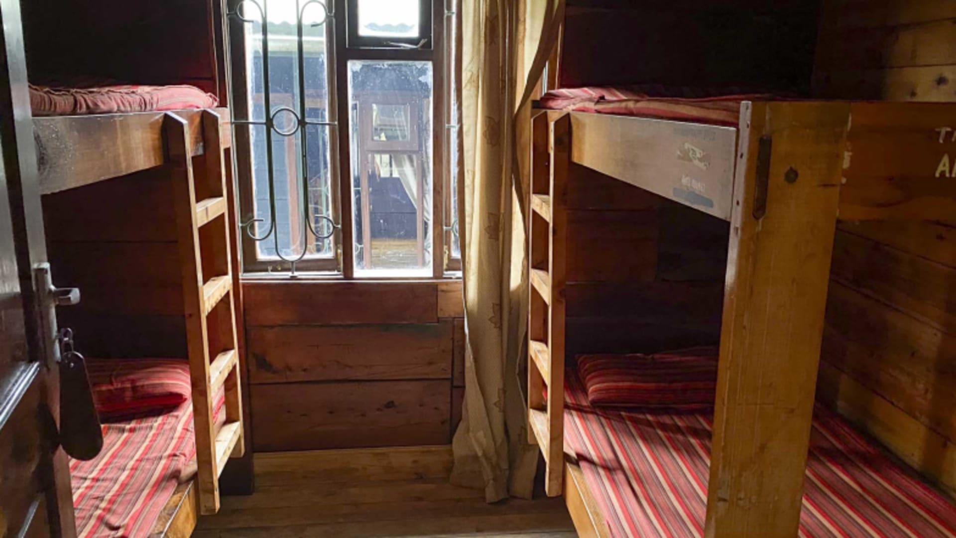 Schlafraum der Sattelhütte (Mt. Meru) mit vier Holzstockbetten und rot-weiß gestreiften Matratzen.