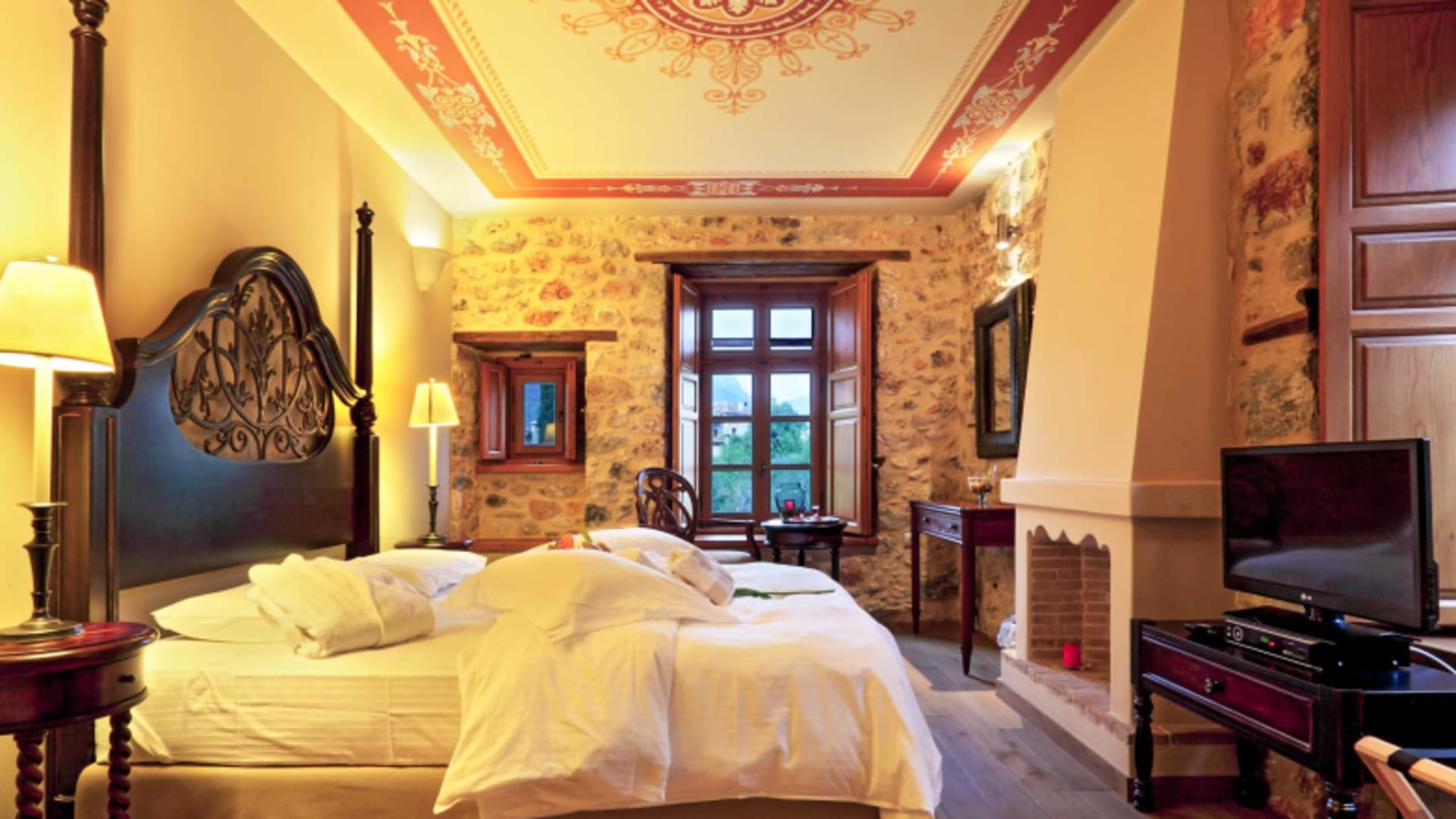 Doppelzimmer im Archontiko Chioti Boutique Hotel mit geschnitztem Holzkopfteil und mediterraner Natursteinwand.