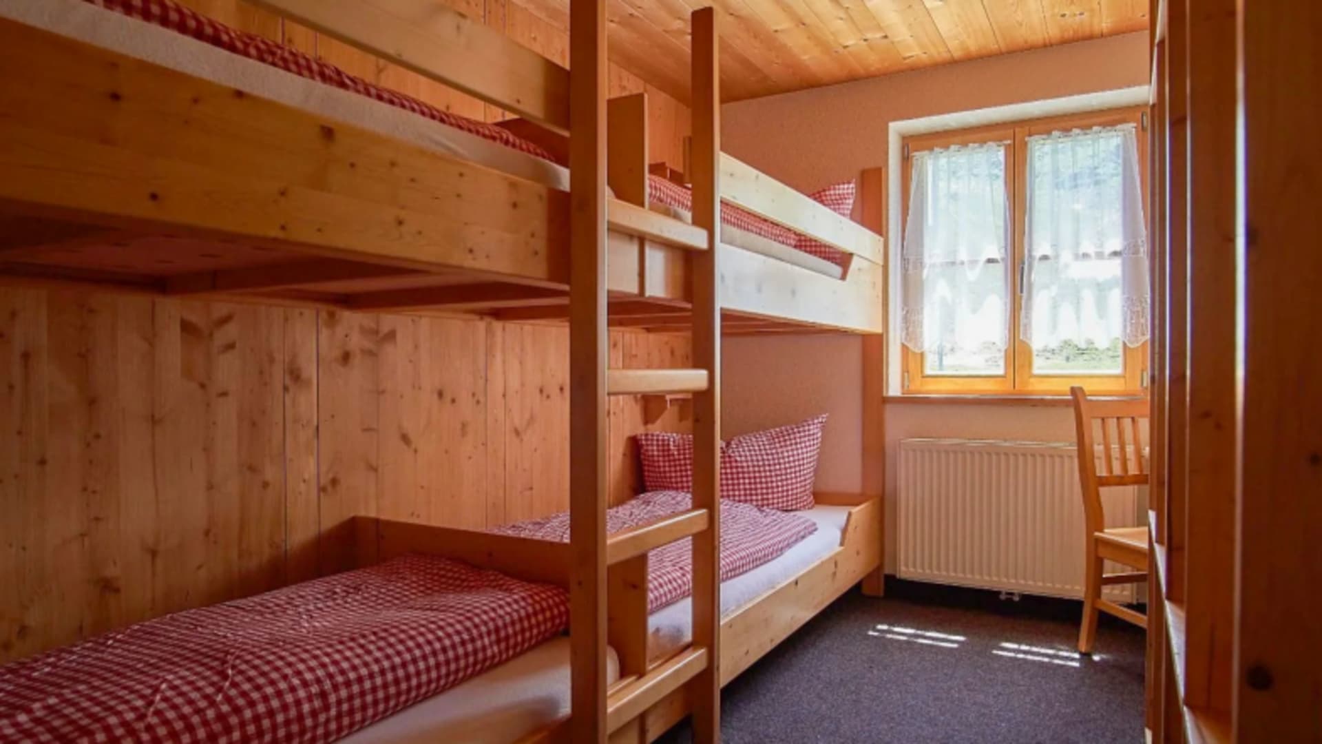 Mehrbettzimmer im Madlenerhaus mit zwei Holz-Etagenbetten und rot-weiß karierter Bettwäsche.
