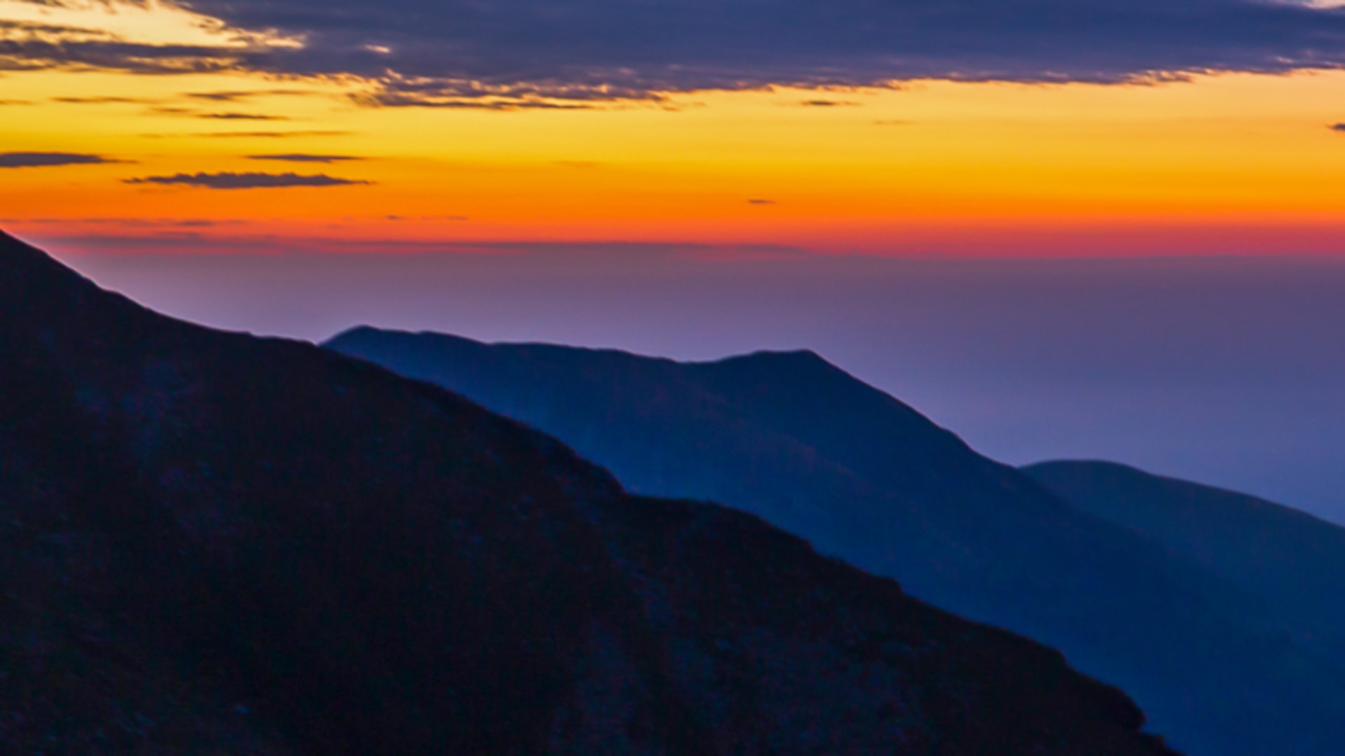 Panoramablick vom Rifugio Rosazza über die Bergketten während der Abenddämmerung mit orangenem und violettem Himmel.