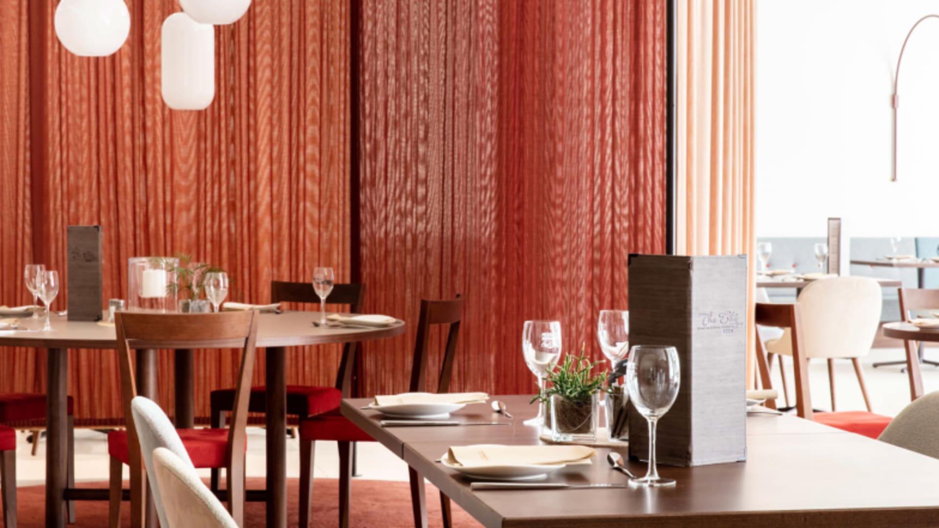 Eingedeckte Tische mit Holzvertäfelung und Pendelleuchten im Restaurant des City Hotel Meran.