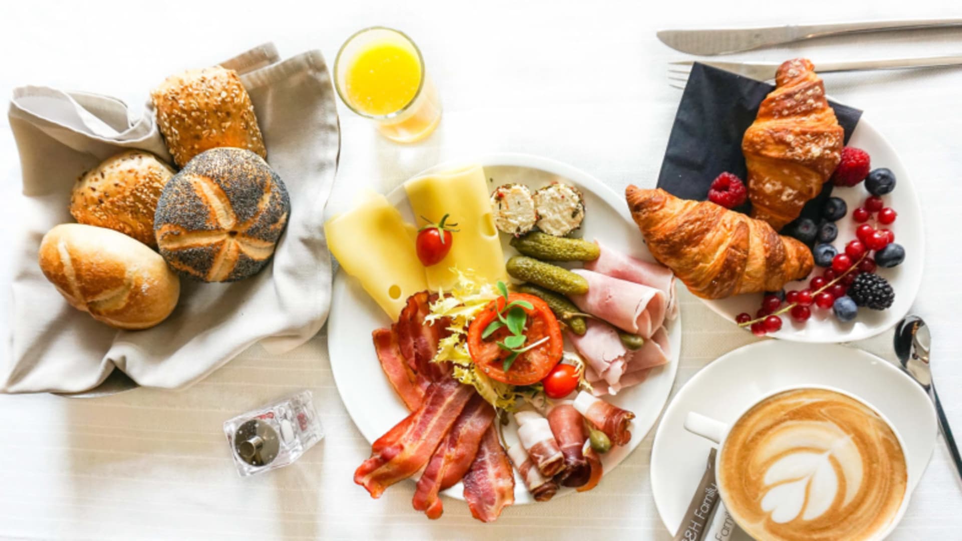 Gedeckter Frühstückstisch mit Brötchen, Aufschnitt und Cappuccino im City Hotel Meran von oben fotografiert.