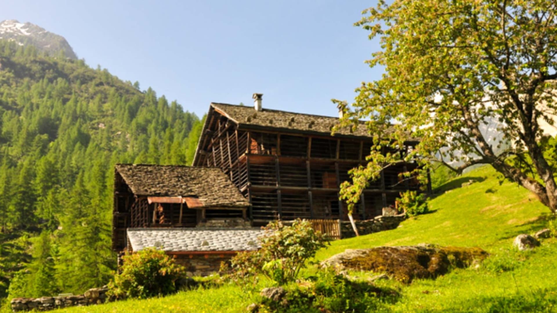 Die Baita Prato della Croce liegt als mehrstöckiges Holzgebäude am grünen Berghang.