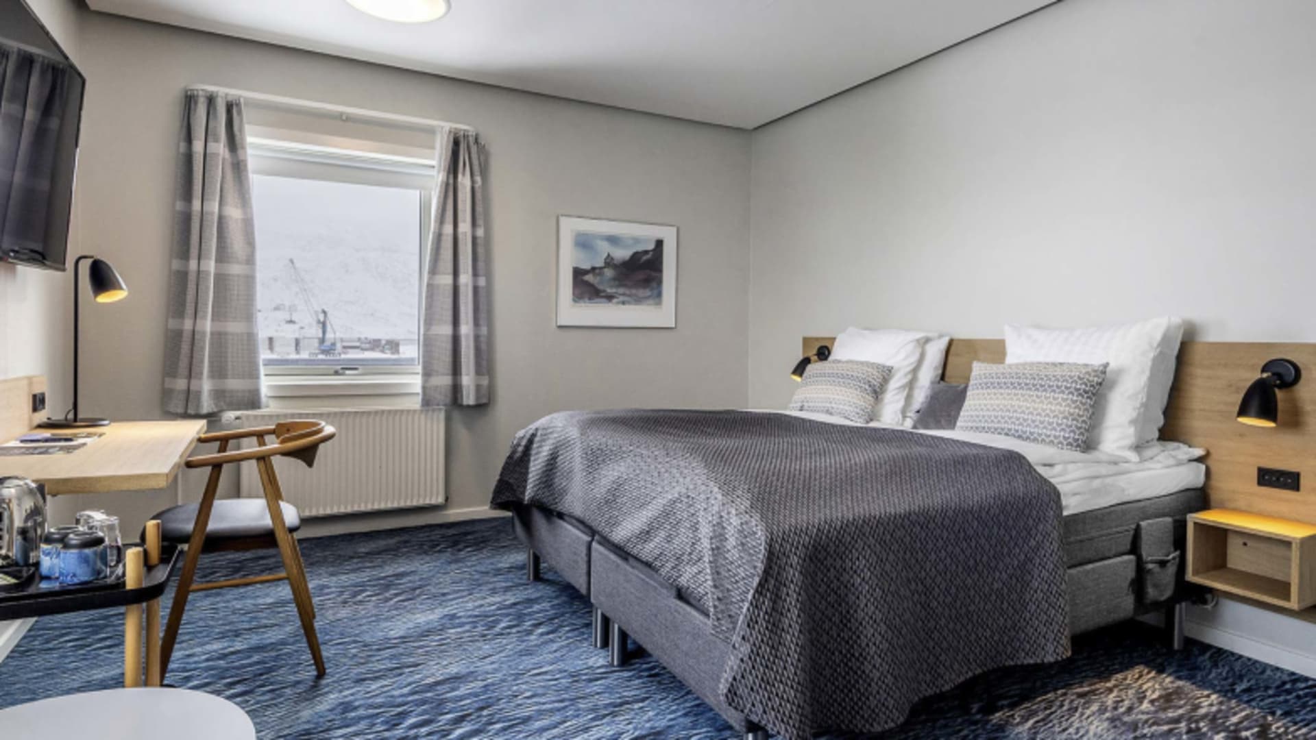 Hotelzimmer im Hotel Søma Nuuk mit Doppelbett und Fensterblick auf verschneite Industrielandschaft von Nuuk.