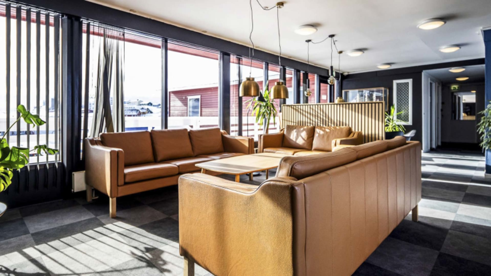 Zentrale Lobby im Hotel Søma Nuuk mit U-förmiger Lederlounge und Blick auf verschneite Landschaft.