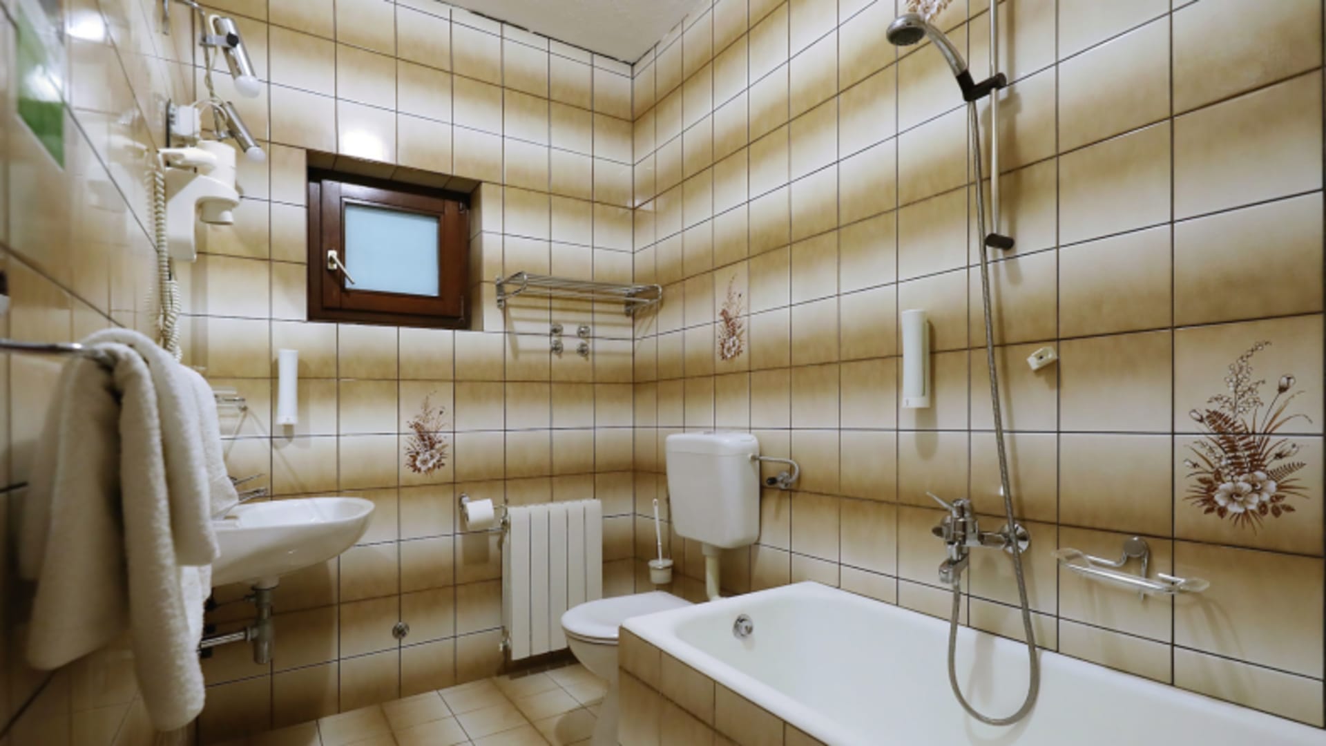 Badezimmer im Hotel Rajna Paklenica mit beigen Fliesen, Badewanne und modernen Sanitäranlagen.