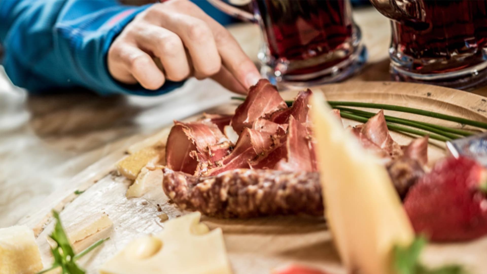Regionale Brotzeit mit Käse und Speck auf Holzbrett in der Zufallhütte bei warmer Innenbeleuchtung.