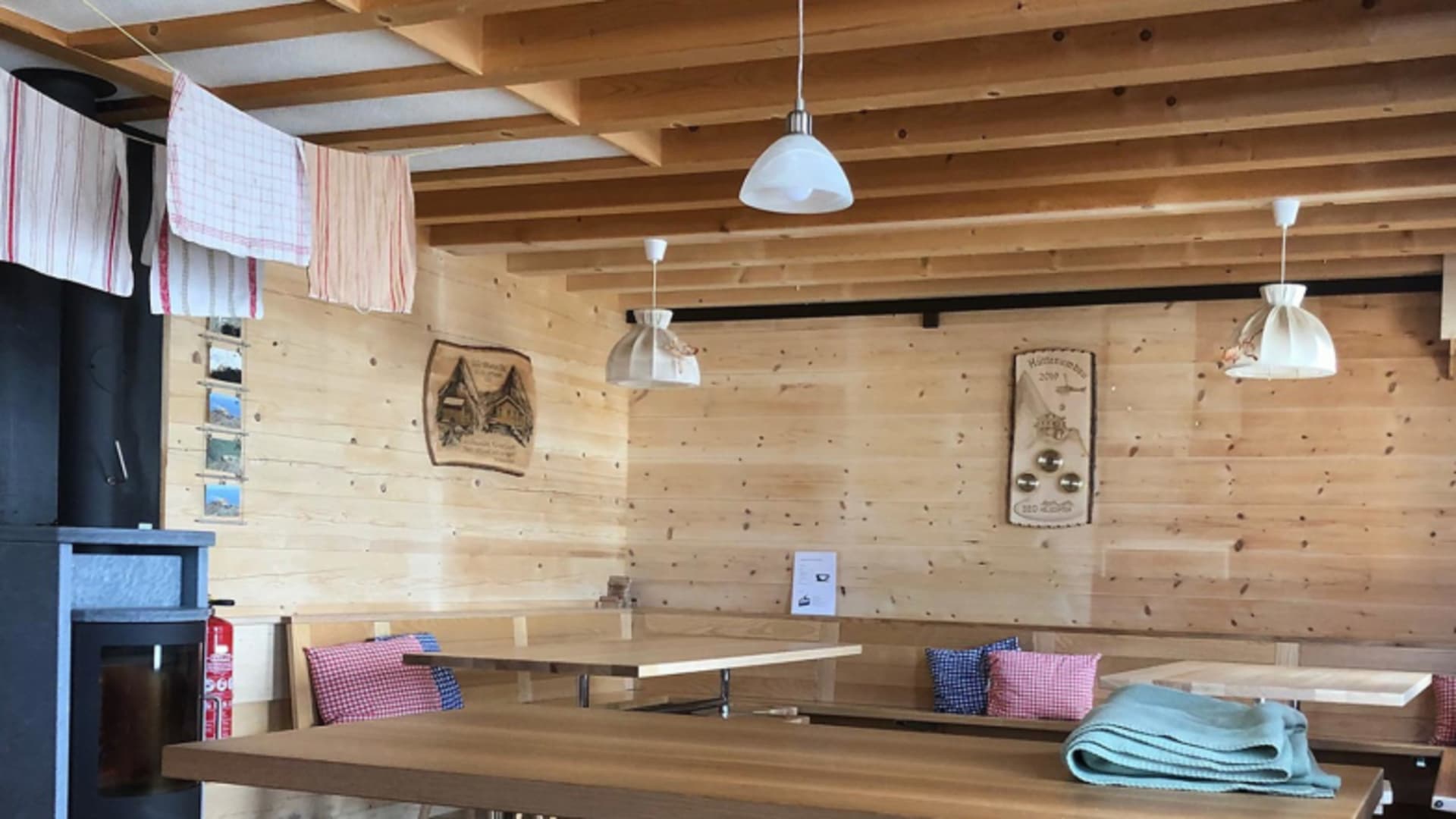 Gastraum der Mittellegihütte mit Holztischen, karierten Sitzkissen und traditioneller Alpeneinrichtung.
