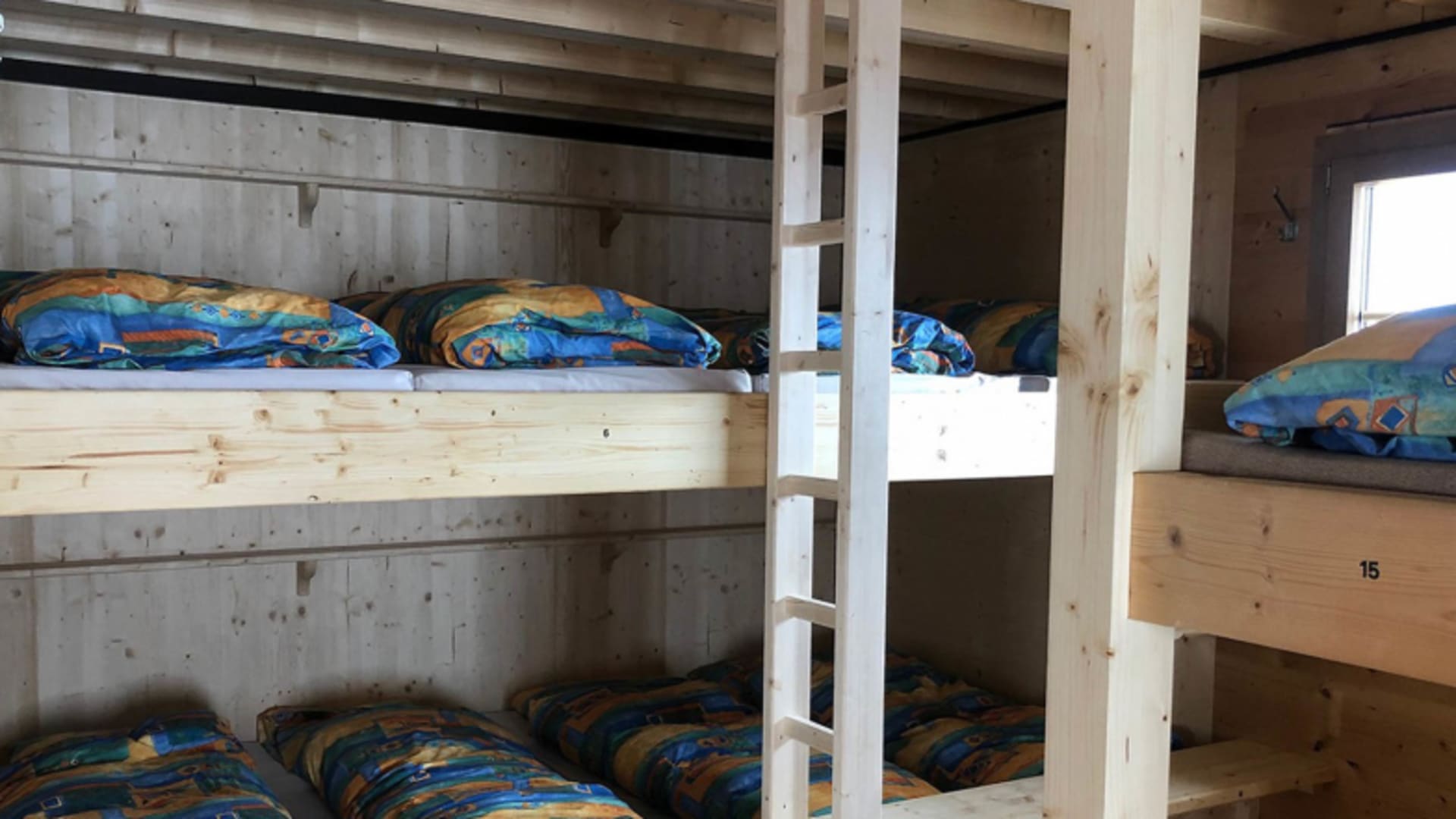 Schlafsaal der Mittellegihütte mit nummerierten Etagenbetten aus Holz und blauen Schlafsäcken.