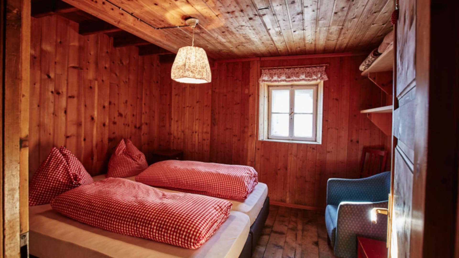Doppelbett mit rot-weiß karierter Bettwäsche in der Schutzhütte Schöne Aussicht / Bella Vista.