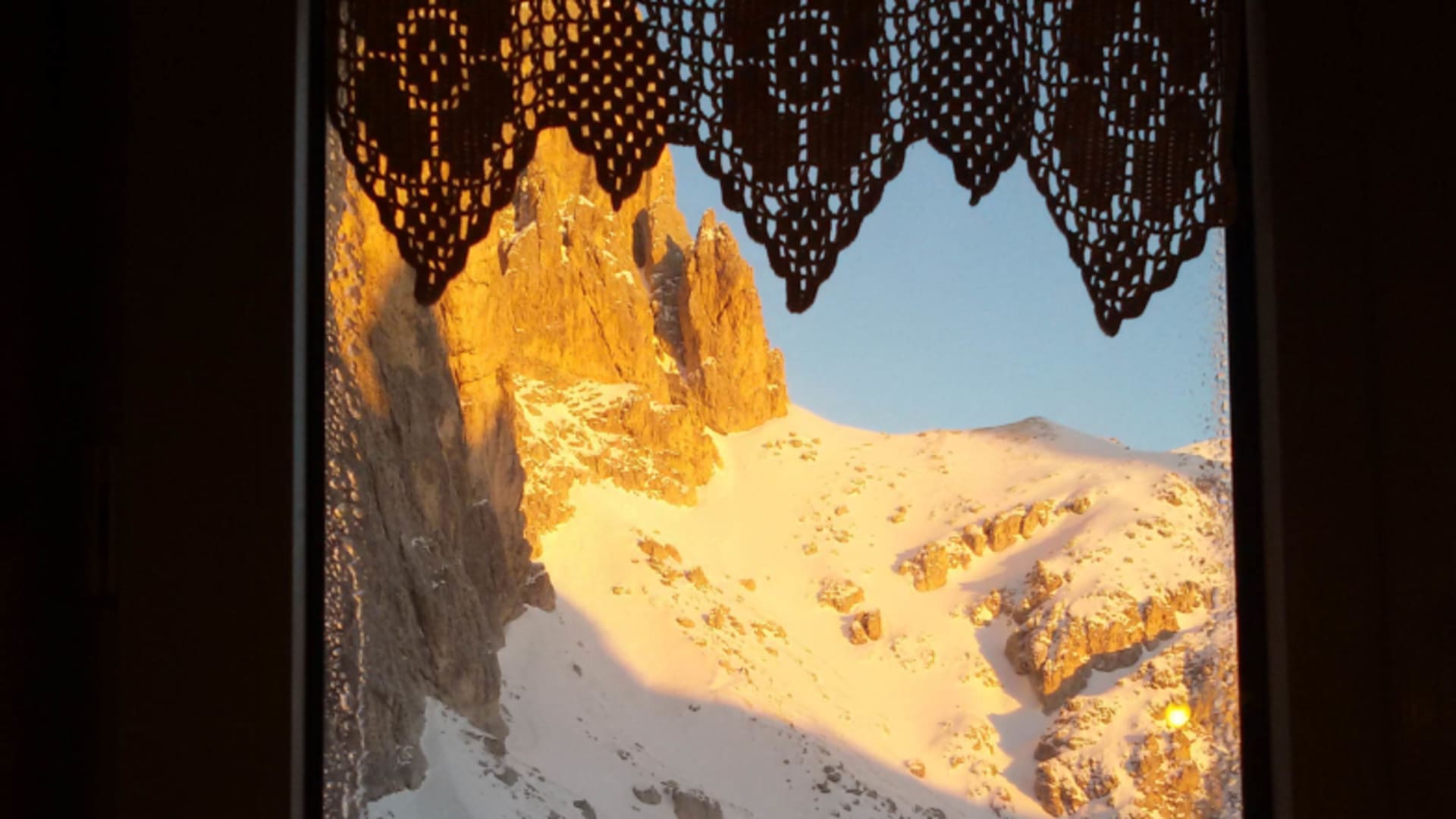 Blick aus dem Fenster der Grasleitenpasshütte auf verschneite Berglandschaft im goldenen Winterlicht.
