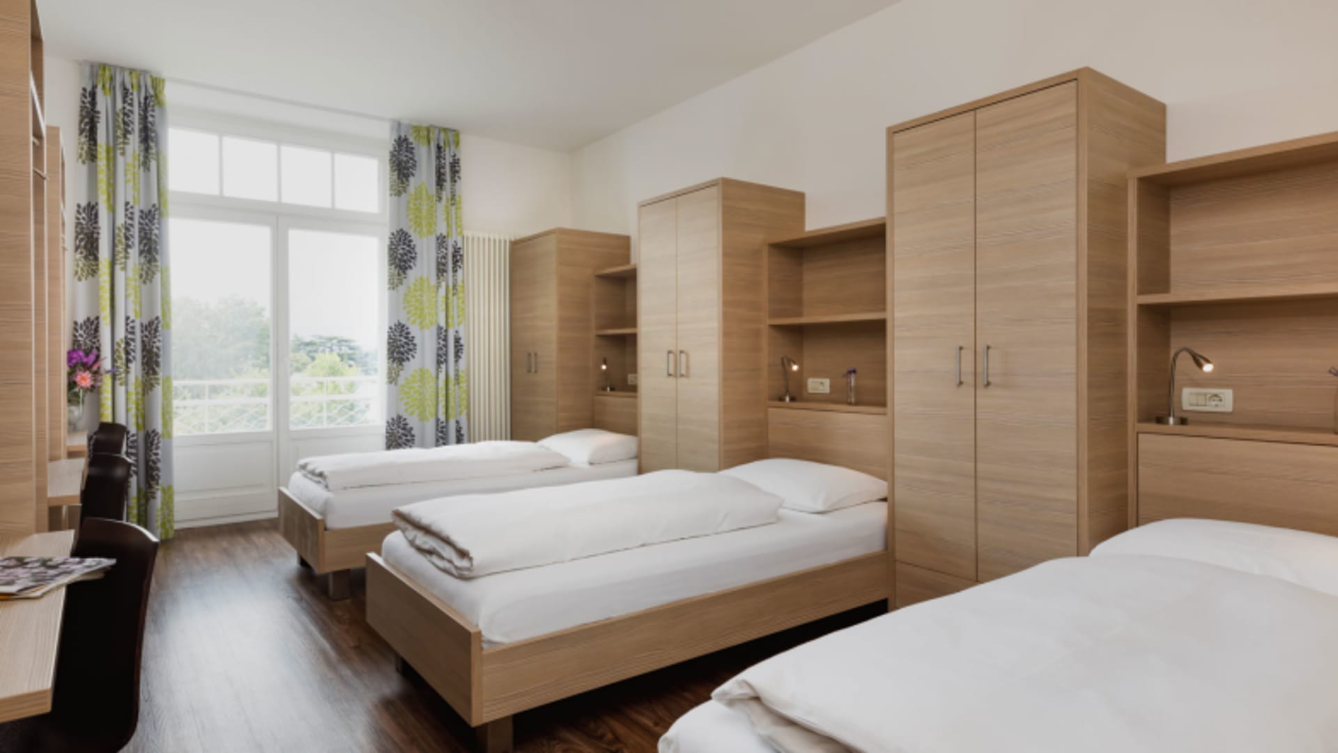 Familienzimmer im Hotel Kolping Meran mit drei Einzelbetten und moderner Holzausstattung für Familien.