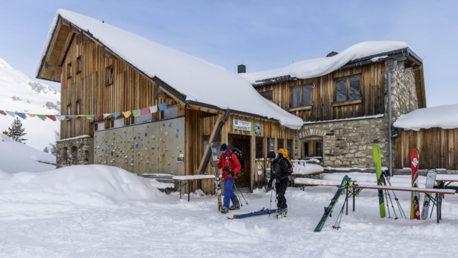 Zwei Skitourengeher mit Skiausrüstung stehen vor der verschneiten Lizumer Hütte in den Tuxer Alpen.