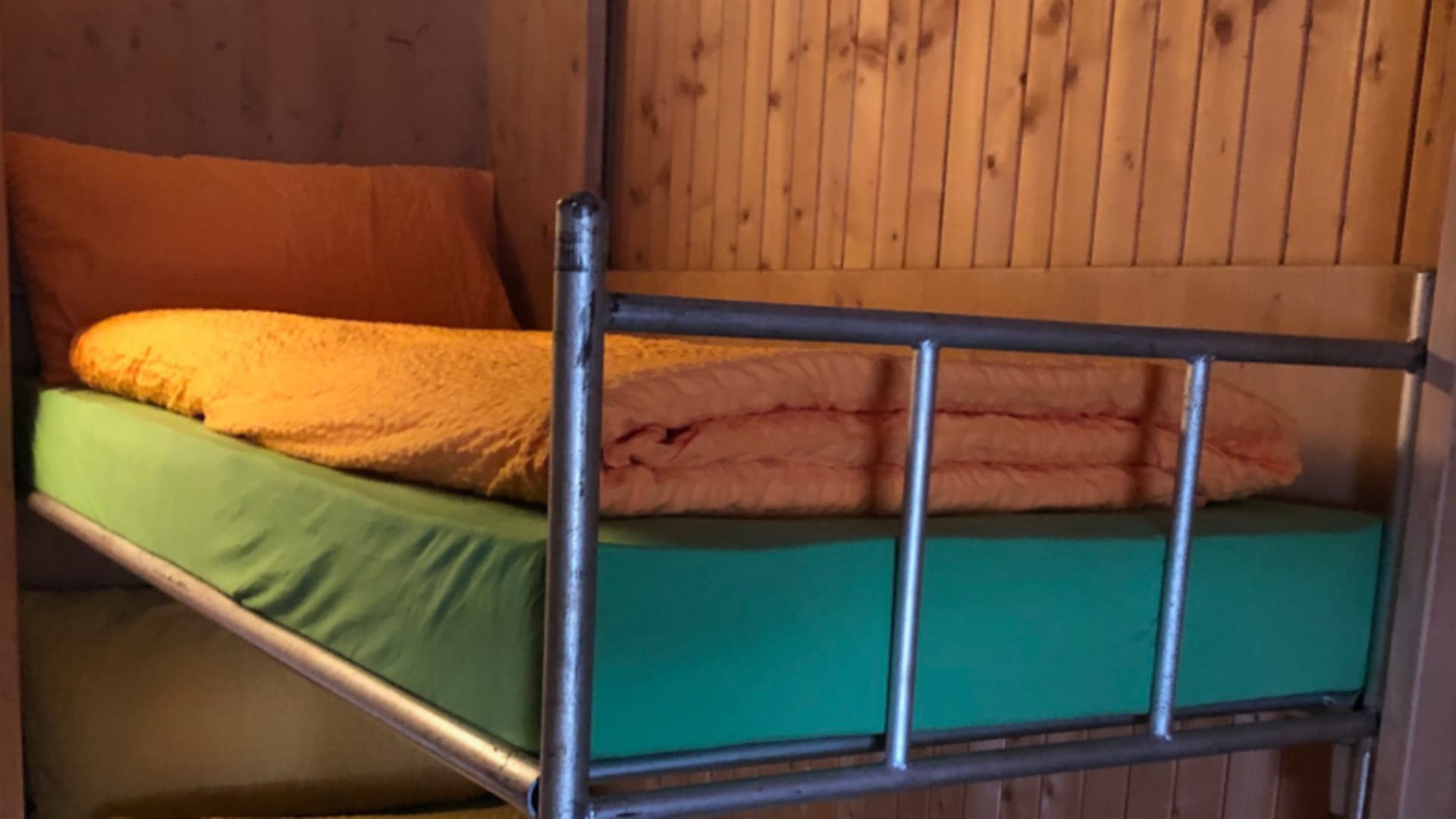 Stockbett im Rifugio Ponti mit bunter Bettwäsche und vollständiger Holzverkleidung der Zimmerwände.
