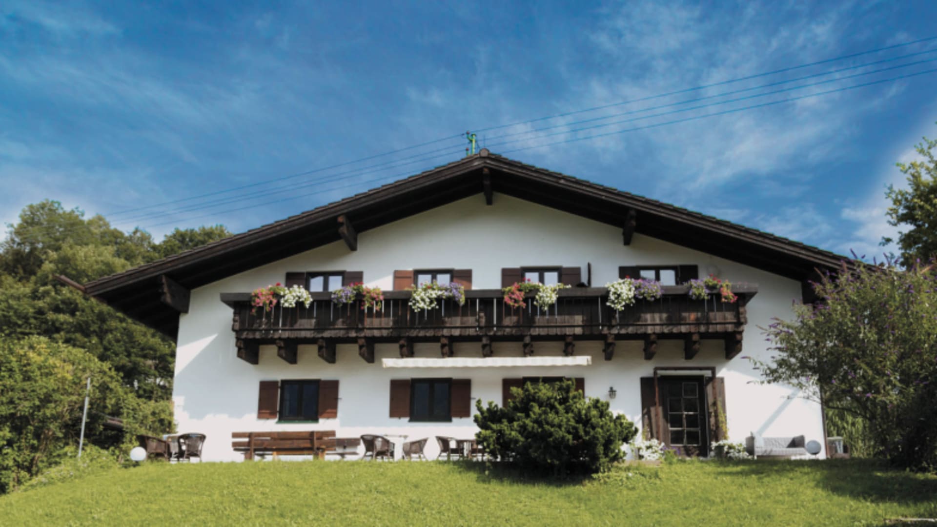 Außenansicht des Berg Blick Hostel mit weißer Fassade, Holzbalkon und Blumenkästen in den Bayerischen Voralpen.