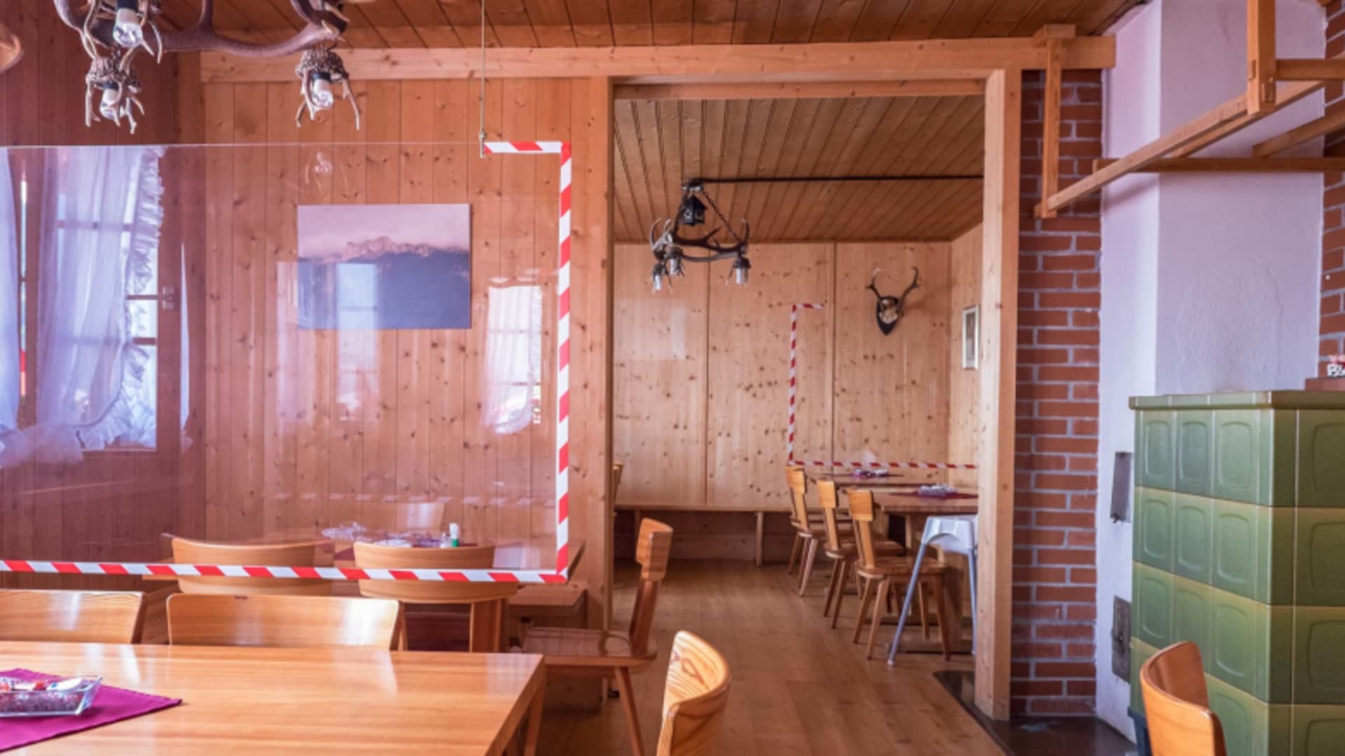 Traditionelle Gaststube der Gafadurahütte mit Kachelofen und Corona-Absperrband zwischen den Tischen.
