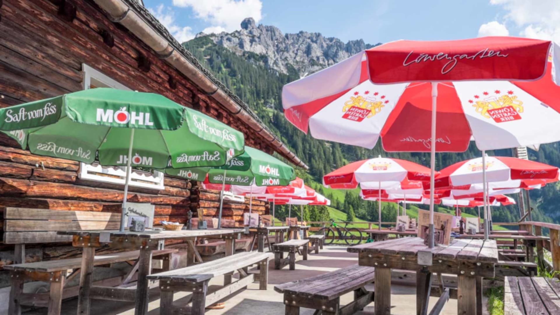 Holzterrasse der Gafadurahütte mit bunten Sonnenschirmen vor der Felswand-Kulisse des Rätikon.