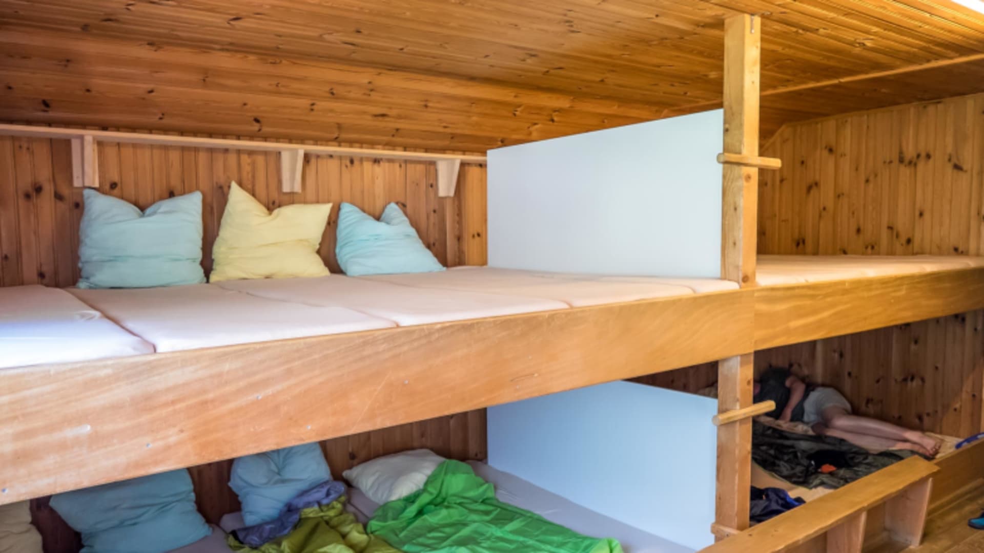 Matratzenlager der Gafadurahütte mit zweistöckigen Holzpritschen und bunter Bettwäsche für Wanderer.