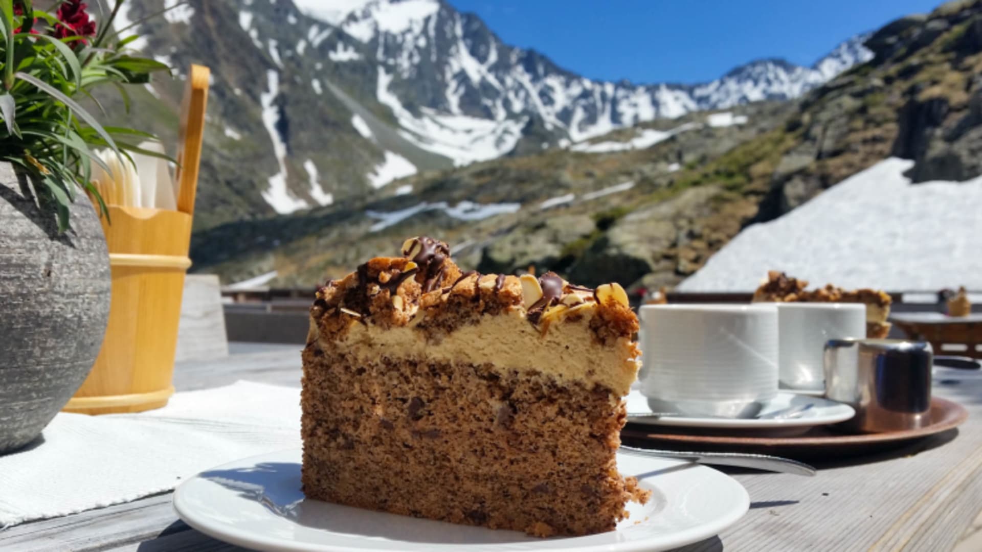 Kuchenstück mit Creme und Nüssen auf der Sonnenterrasse der Nürnberger Hütte mit Bergpanorama der Stubaier Alpen.