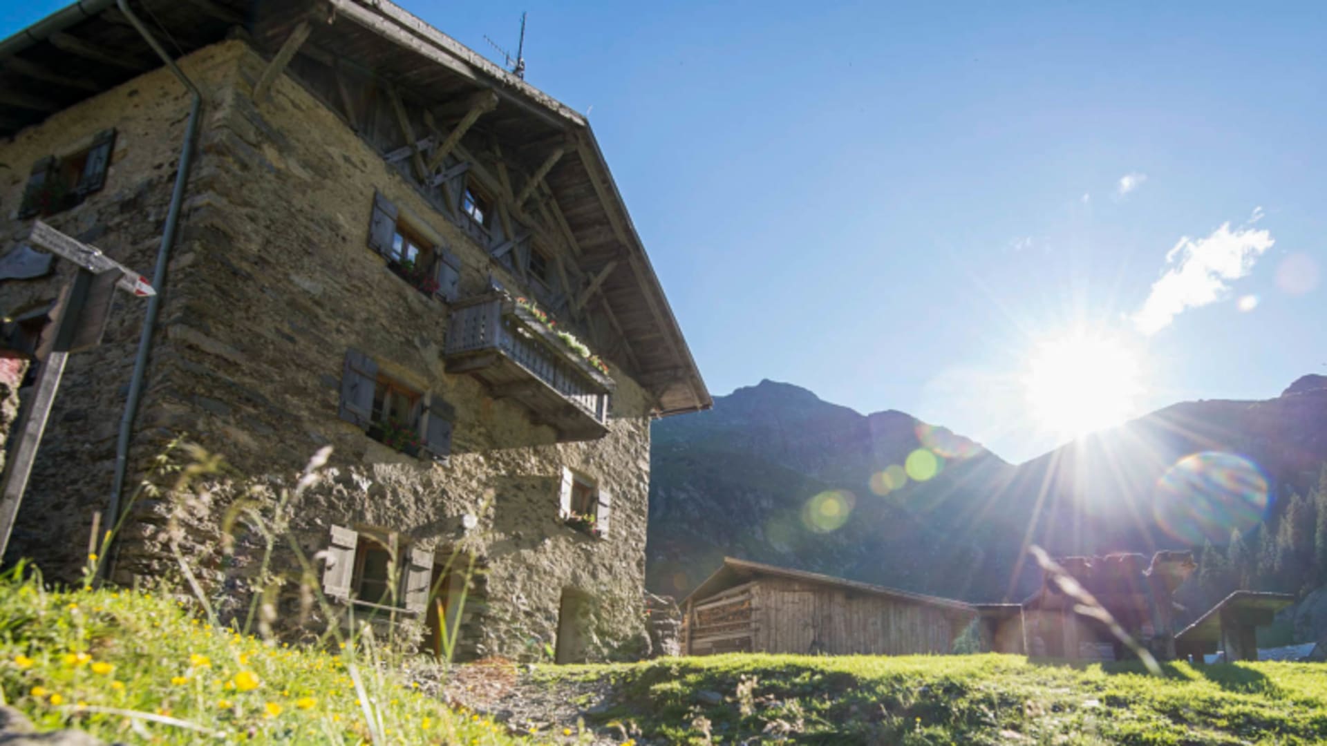 Schutzhaus Bockerhütte aus Naturstein mit Holzbalkon inmitten grüner Almwiesen.