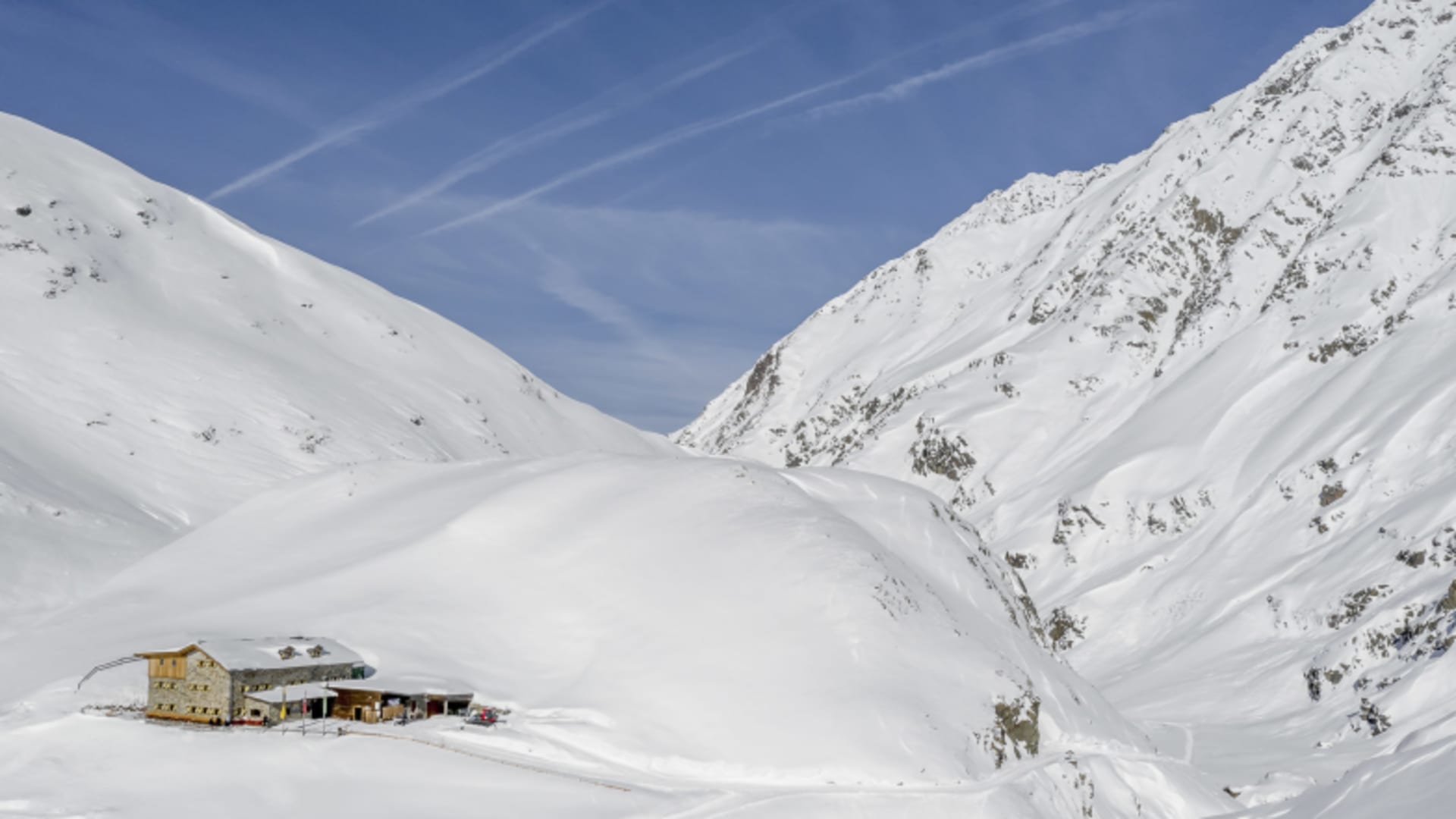 Die Amberger Hütte steht isoliert in verschneiter Hochebene der Stubaier Alpen umgeben von Gipfeln.