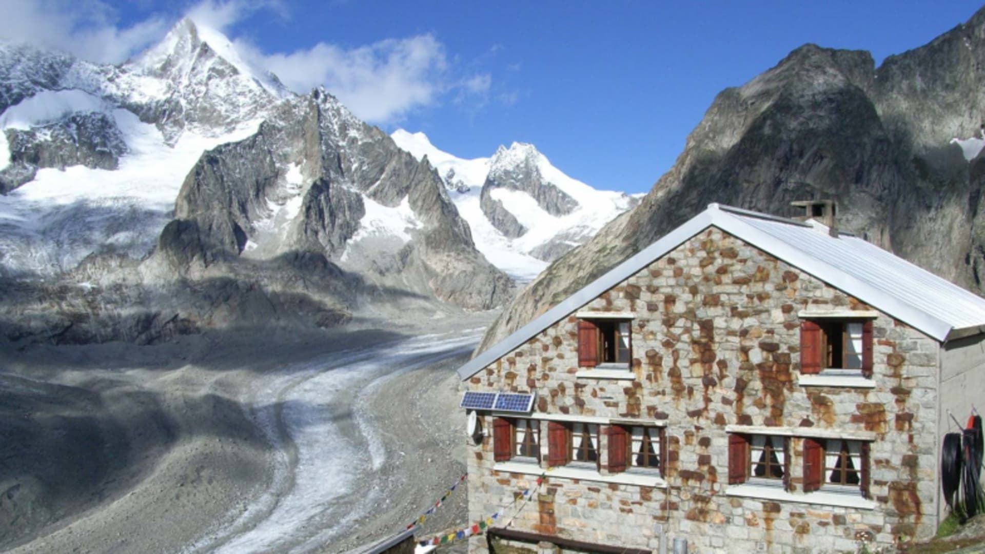 Außenansicht der Oberaletschhütte aus Naturstein mit Solarpanels und Gletscherblick in hochalpiner Lage der Berner Alpen.
