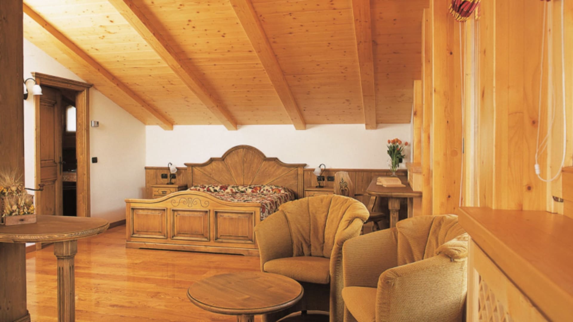 Hotelsuite im Hotel SPÖL Livigno mit Holzbalkendecke, Doppelbett und Polstersesseln.