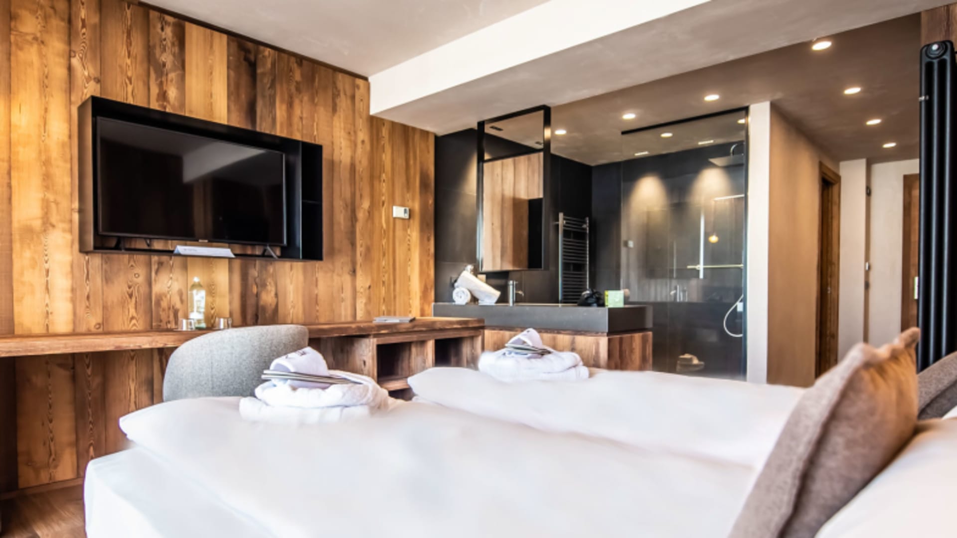 Modernes Hotelzimmer im Hotel SPÖL Livigno mit Holzwand und offenem Badezimmer.