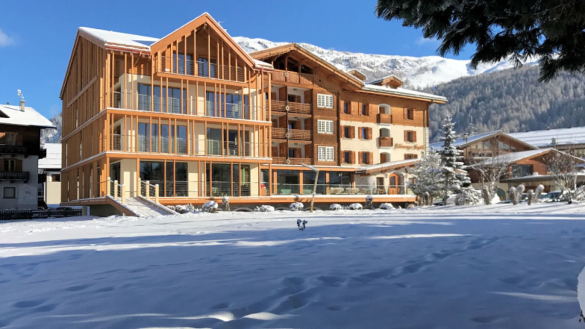 Winteransicht des Hotel SPÖL Livigno mit Holzfassade vor schneebedeckten Berghängen.