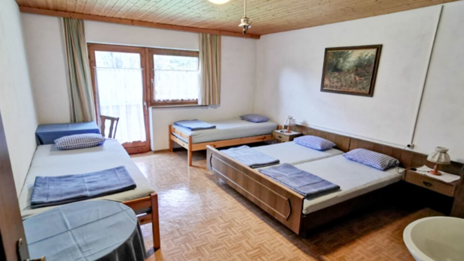 Das Mehrbettzimmer der Gaistalalm bietet drei Einzelbetten mit blauer Bettwäsche unter einer rustikalen Holzdecke.