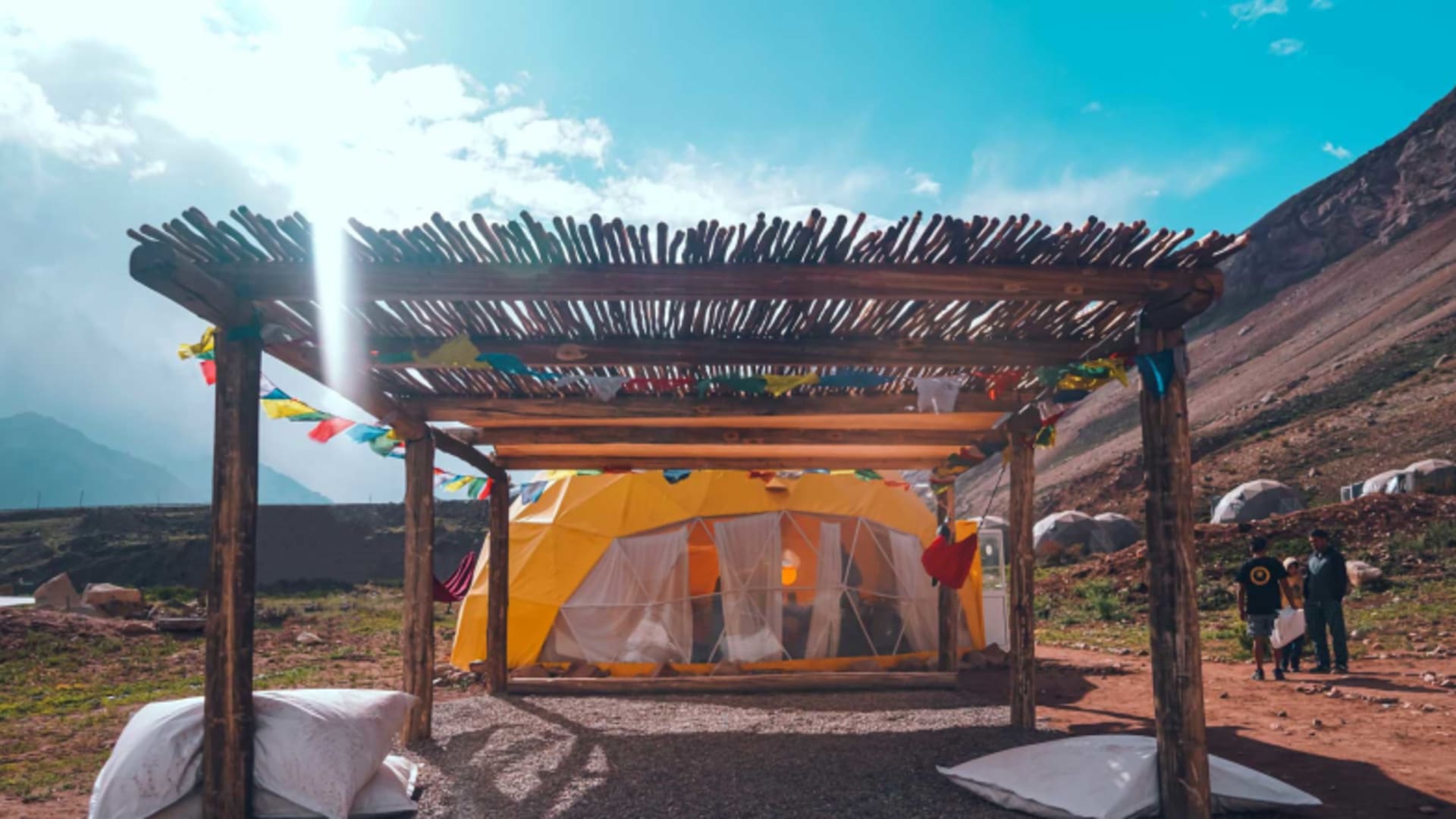 Die Inca Ranch zeigt ein orangefarbenes Expeditionszelt unter Holzkonstruktion mit Gebetsfahnen in karger Berglandschaft.