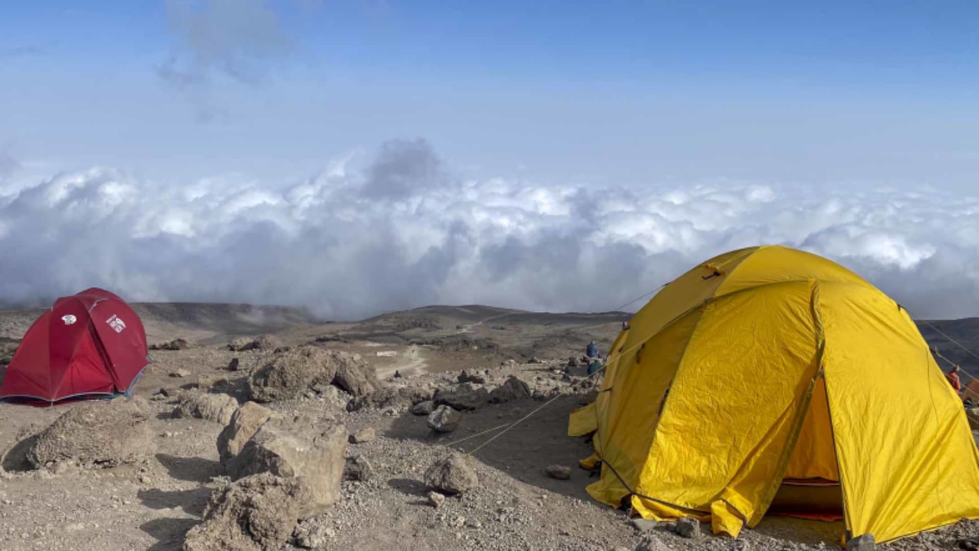 Gelbe und rote Expeditionszelte auf steinigem Vulkangestein im Zeltcamp am Kilimanjaro bei bewölktem Himmel.