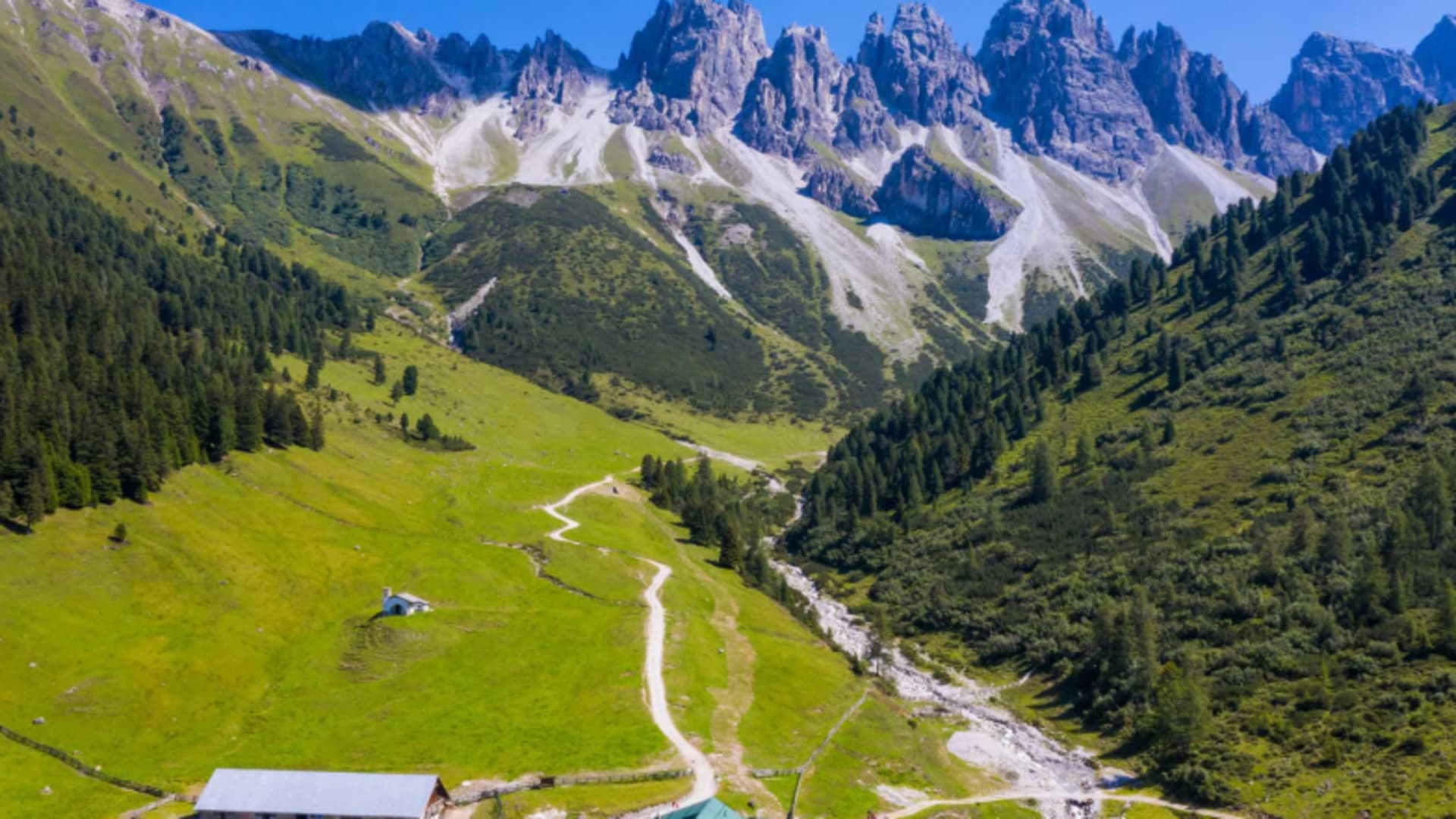 Luftaufnahme der Kemater Alm im Hochtal mit Wanderweg, grünen Almwiesen und steilen Felswänden ringsum.