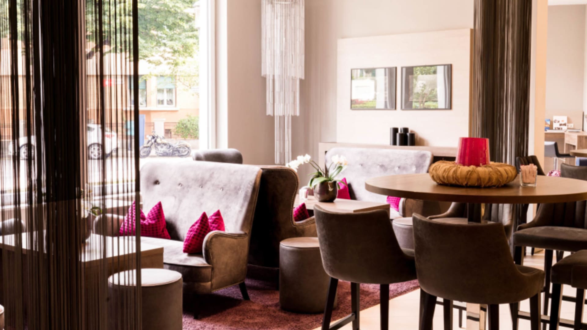 Lounge-Bereich mit Lederstühlen und Holztisch im City Hotel Meran mit Fensterblick nach draußen.
